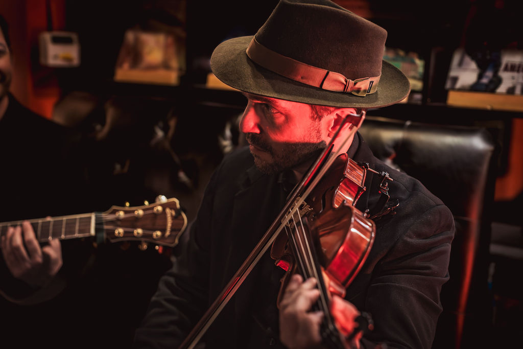 Joseph Arnold in fedora, red-lit close-up with guitar in foreground